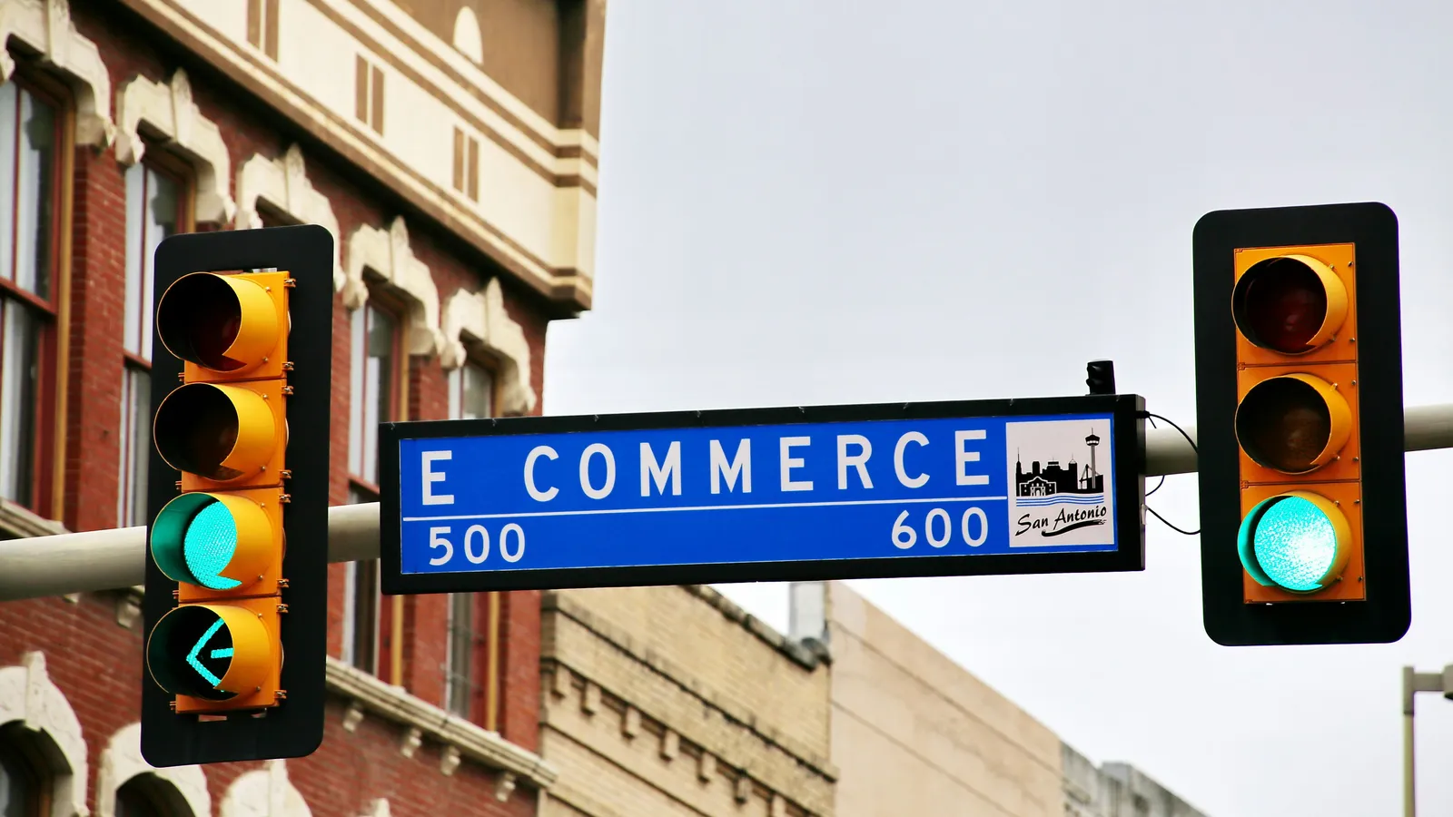 An E Commerce street sign between green traffic lights.